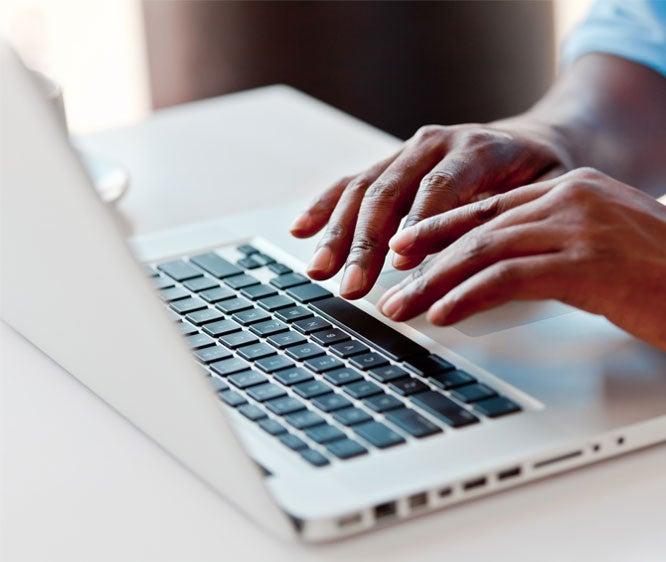 A close up shot of a Black person typing on a laptop.