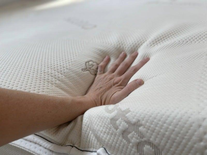 A person presses down on the Saatva mattress topper