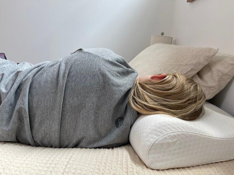 A woman lays on her side using the TEMPUR-Neck pillow.