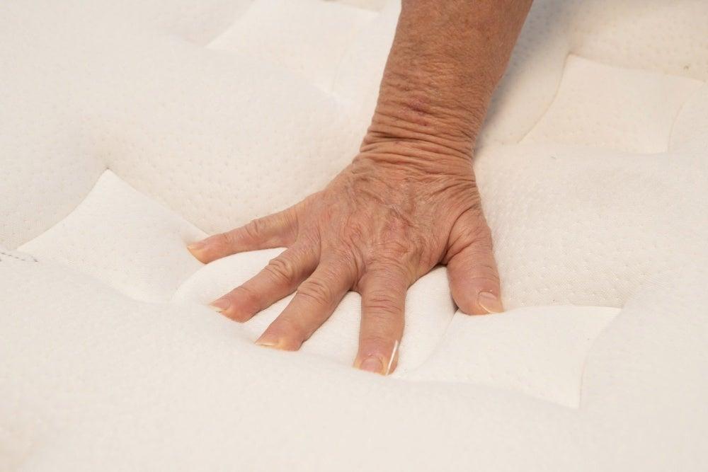 A hand pushes down on the top of a plush mattress