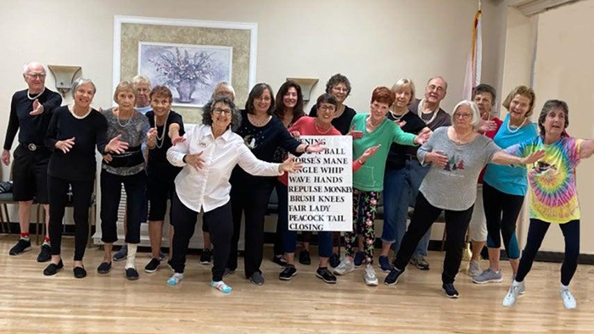 A group of people smile at the camera and pose following a Tai Chi class.