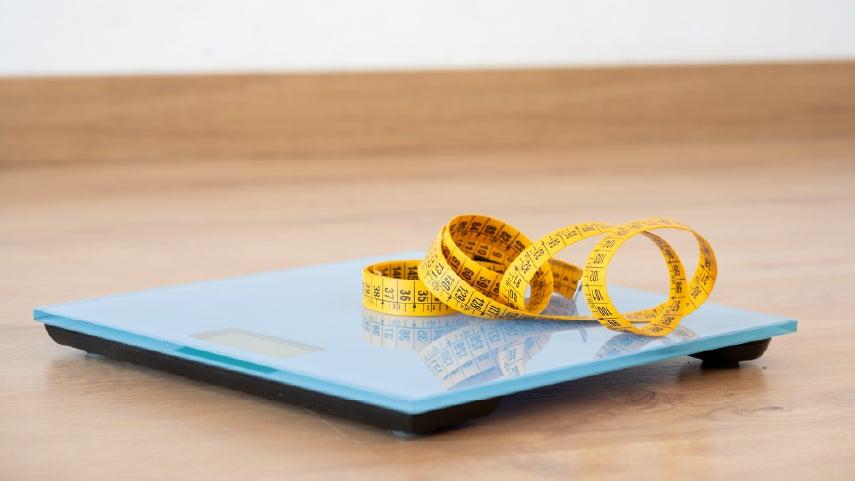A measuring tape sits on top of a digital weight scale.
