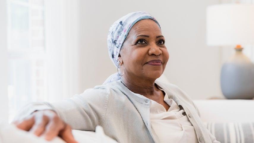 A Black senior woman cancer survivor is sitting on a couch looking grateful.